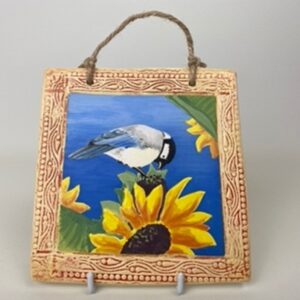 A handmade earthenware hanging wall tile. This tile design of a blue tit on a sunflower symbolise a  cheerful and sunny nature. 