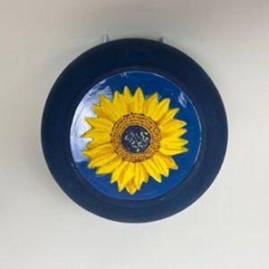 A handmade earthenware fruit bowl, with the rim colored in green and the body colored in deep blue. A secret painted sunflower is on the inside. 